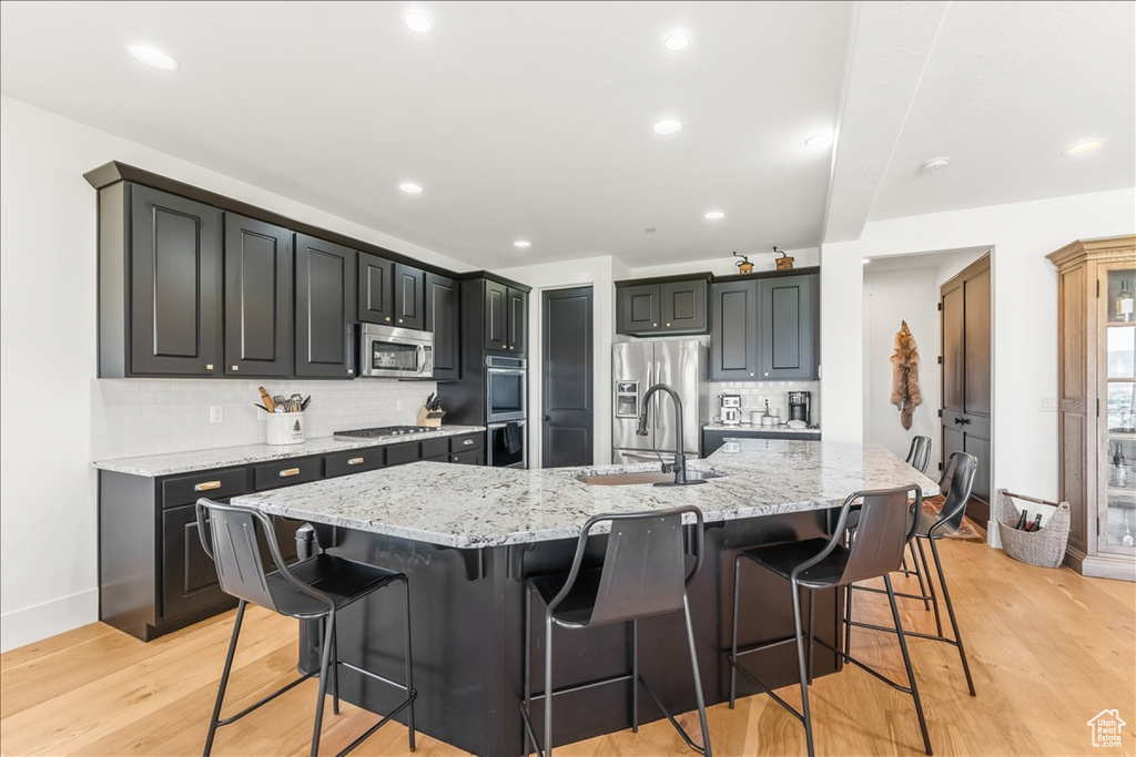 Kitchen featuring light hardwood / wood-style floors, appliances with stainless steel finishes, a large island with sink, and tasteful backsplash