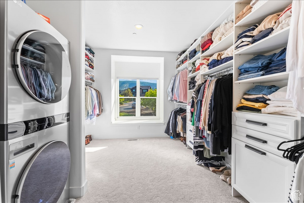 Walk in closet with light carpet and stacked washer and dryer