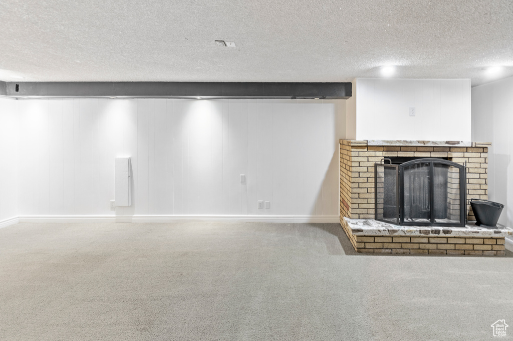 Unfurnished living room with a brick fireplace, carpet floors, and a textured ceiling