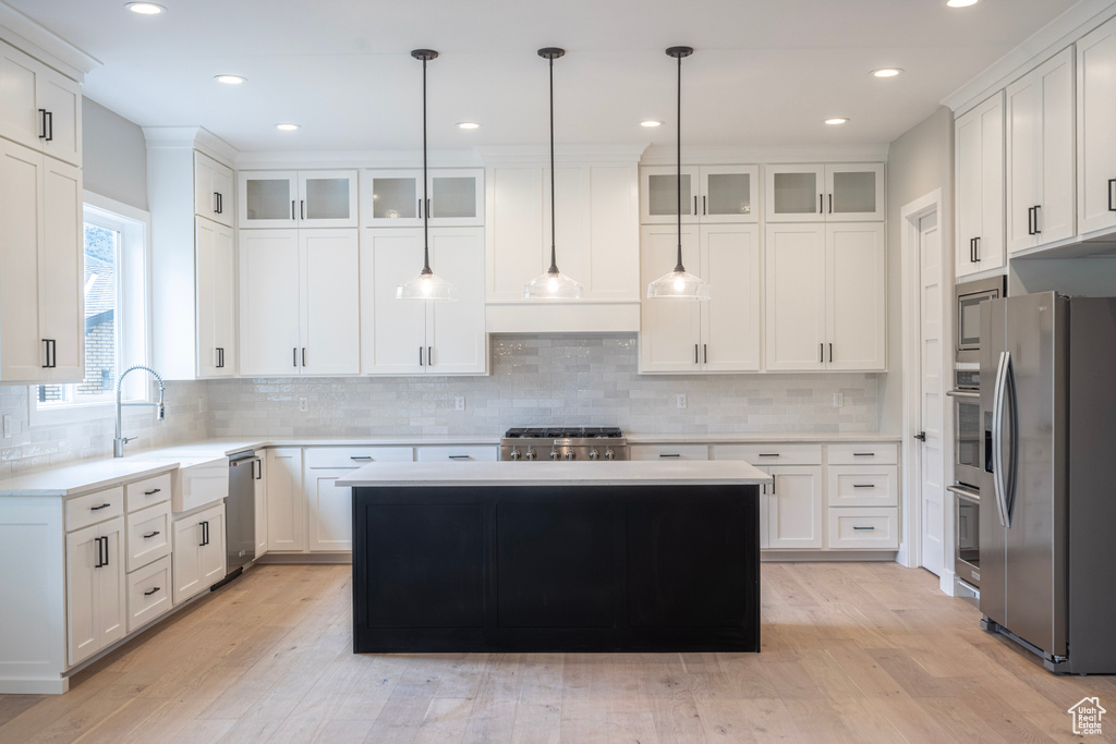 Kitchen with appliances with stainless steel finishes, light hardwood / wood-style floors, tasteful backsplash, white cabinetry, and a center island