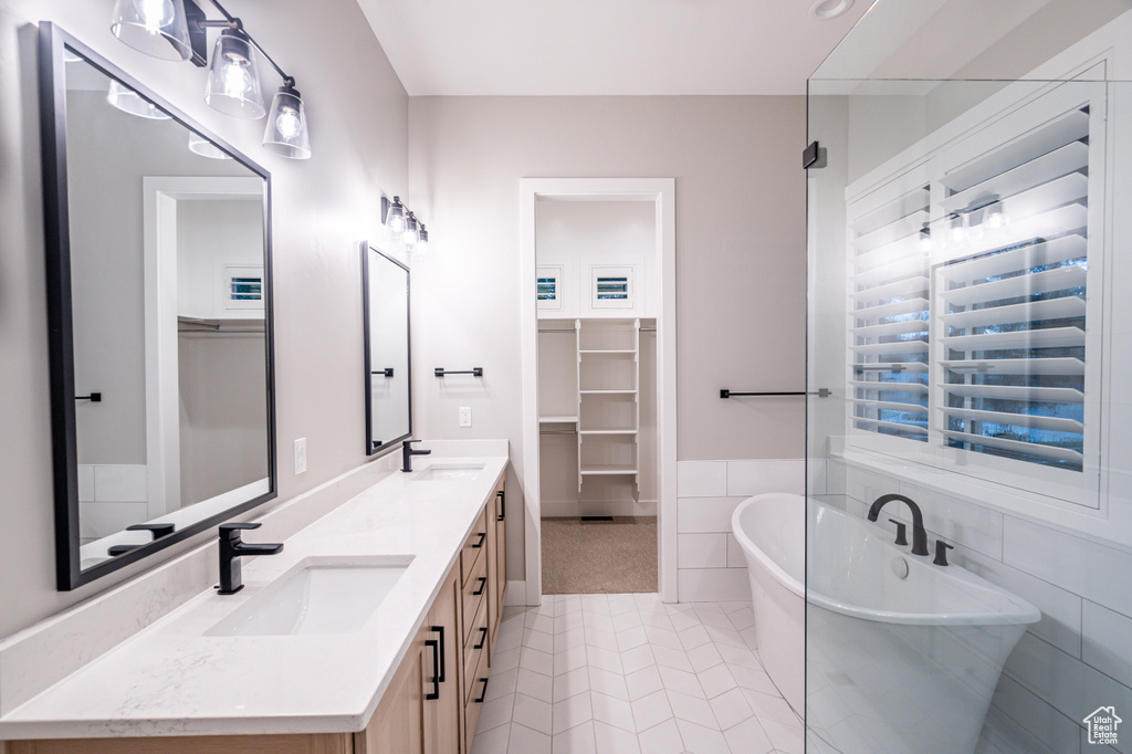 Bathroom featuring tile floors, tile walls, a bath, double sink, and oversized vanity