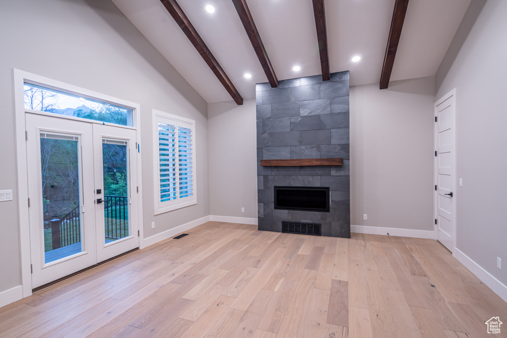 Unfurnished living room featuring light hardwood / wood-style flooring, french doors, lofted ceiling with beams, and a fireplace