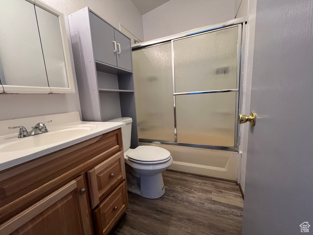 Full bathroom with wood-type flooring, vanity, toilet, and bath / shower combo with glass door