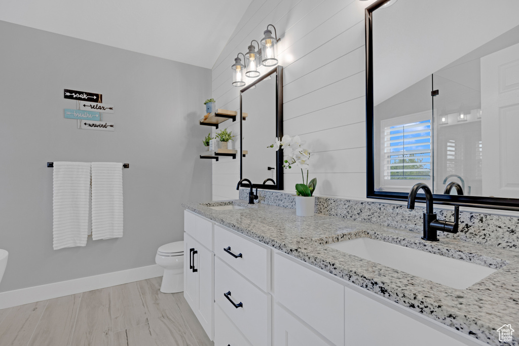 Bathroom featuring dual sinks, vaulted ceiling, toilet, and large vanity