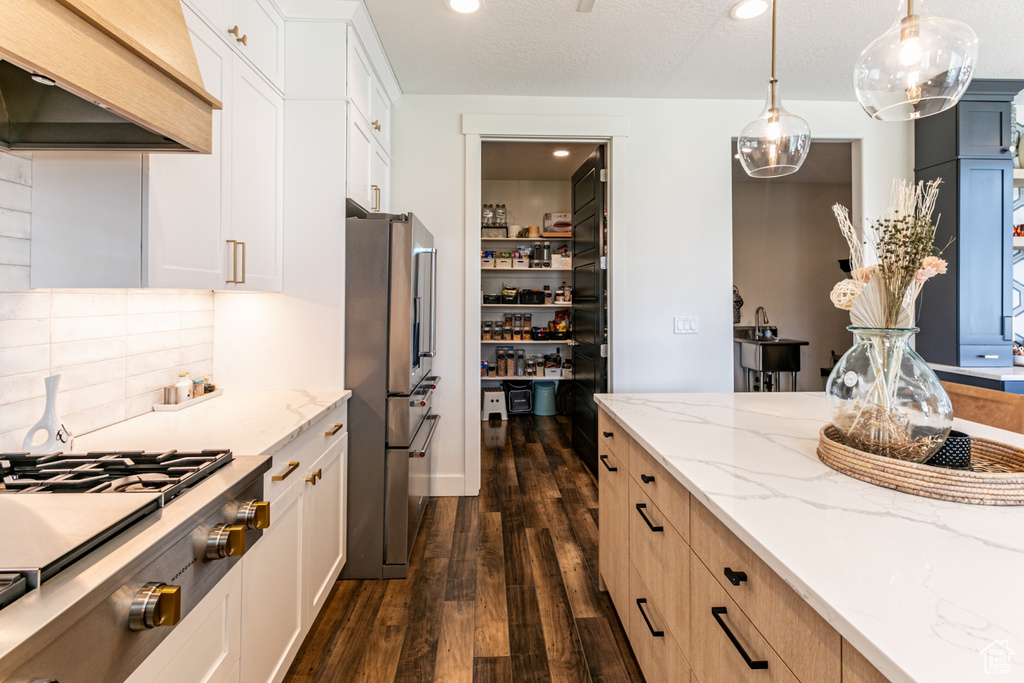 Kitchen featuring light stone counters, backsplash, dark hardwood / wood-style floors, stainless steel fridge with ice dispenser, and custom range hood
