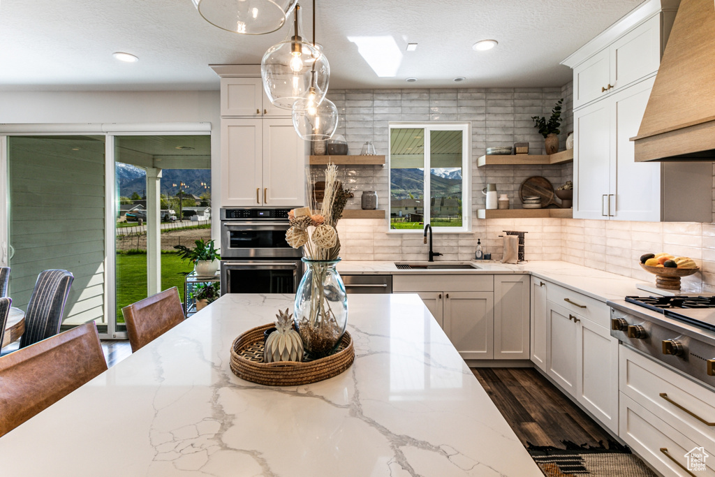 Kitchen featuring hanging light fixtures, dark hardwood / wood-style floors, backsplash, custom range hood, and sink