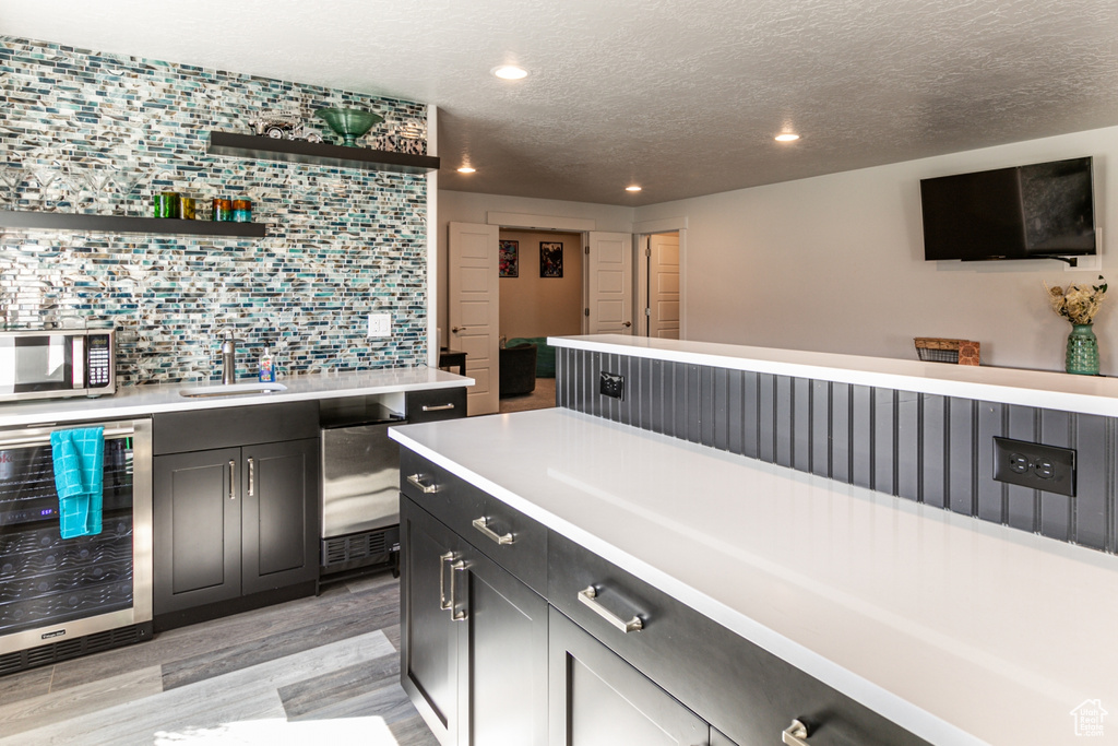 Kitchen with beverage cooler, sink, tasteful backsplash, light hardwood / wood-style floors, and a textured ceiling