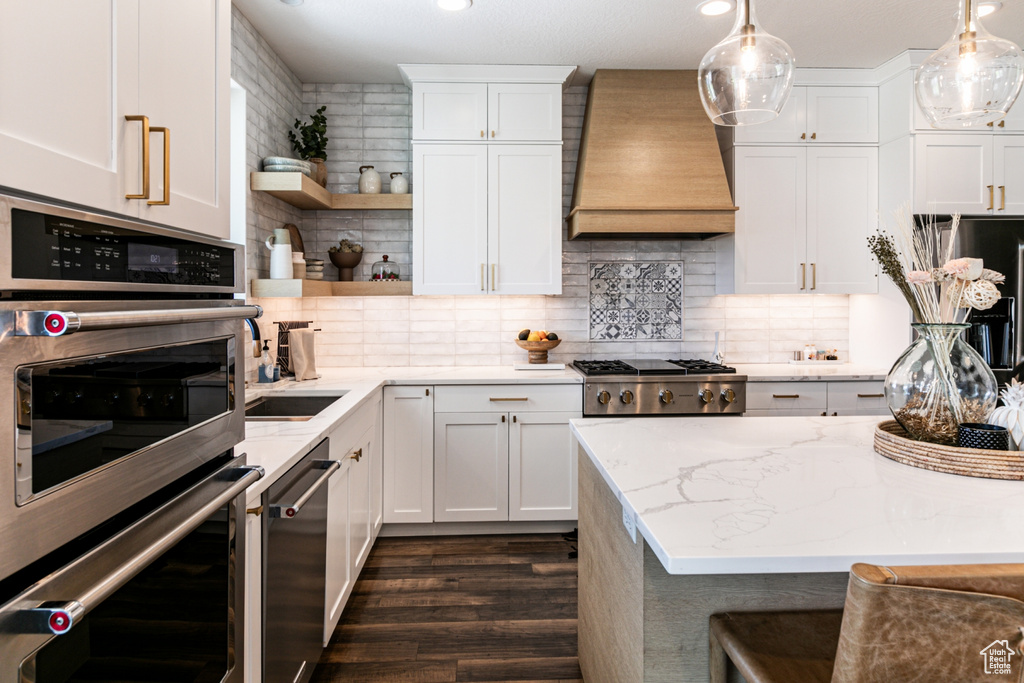 Kitchen with premium range hood, double oven, tasteful backsplash, and decorative light fixtures