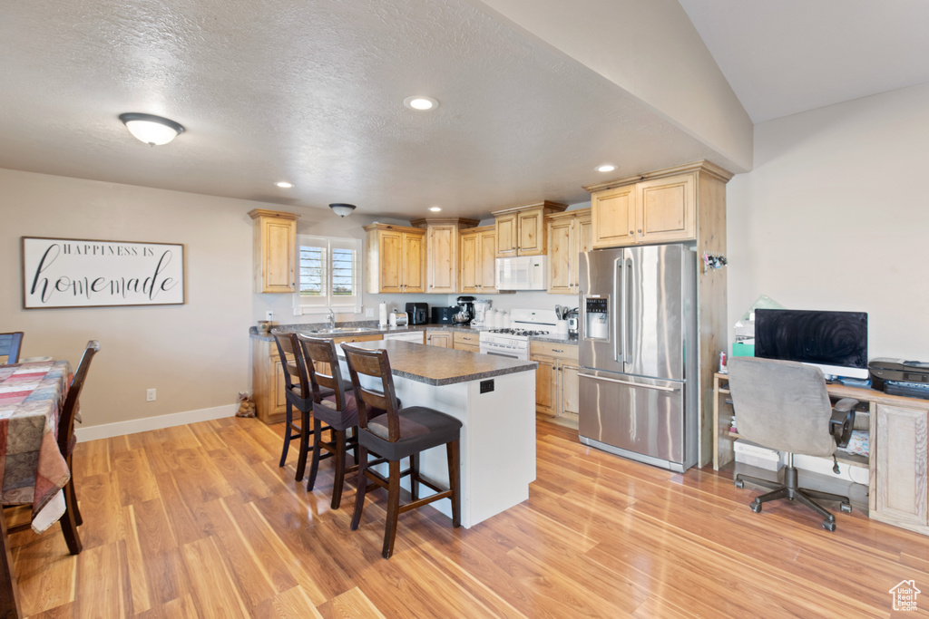 Kitchen with light brown cabinets, a kitchen island, a breakfast bar area, white appliances, and light hardwood / wood-style floors