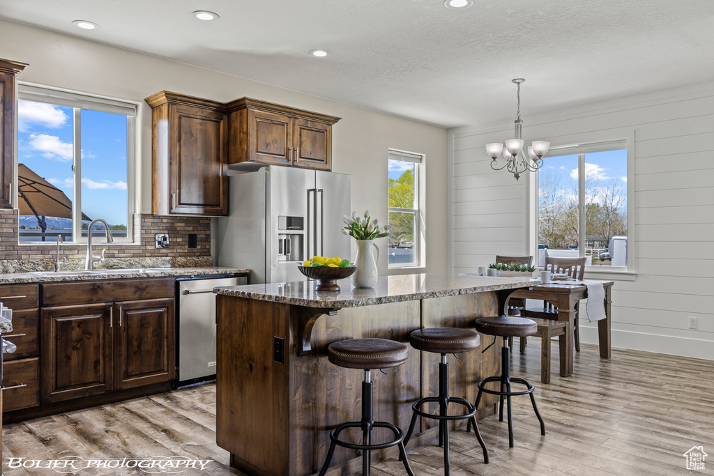 Kitchen with decorative light fixtures, a kitchen island, stainless steel appliances, sink, and light wood-type flooring