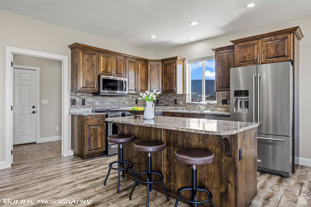 Kitchen featuring light stone countertops, appliances with stainless steel finishes, light hardwood / wood-style flooring, tasteful backsplash, and a center island