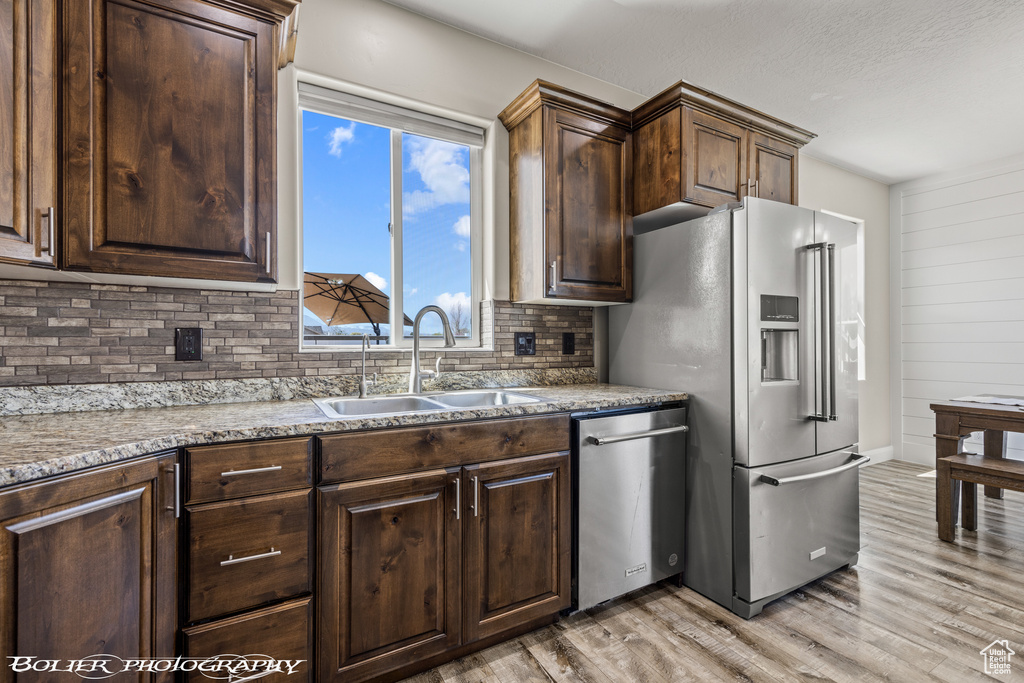 Kitchen featuring stone countertops, appliances with stainless steel finishes, sink, light hardwood / wood-style floors, and backsplash