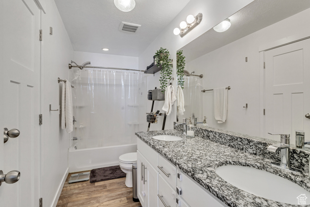 Full bathroom featuring dual vanity, hardwood / wood-style floors, shower / tub combo with curtain, and toilet