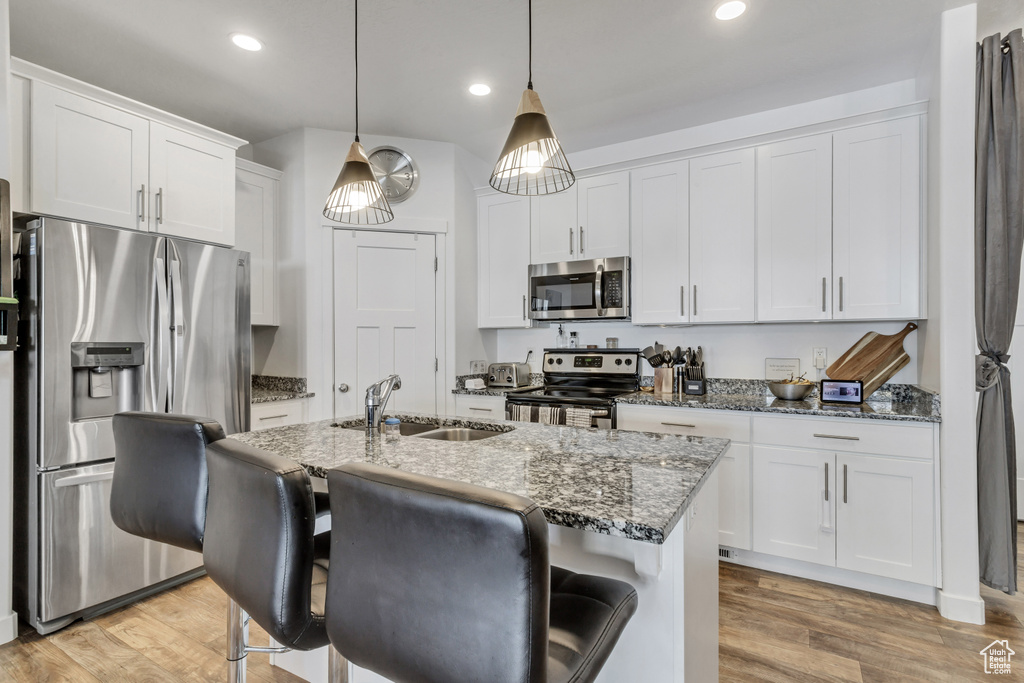 Kitchen with pendant lighting, appliances with stainless steel finishes, white cabinets, sink, and light hardwood / wood-style floors