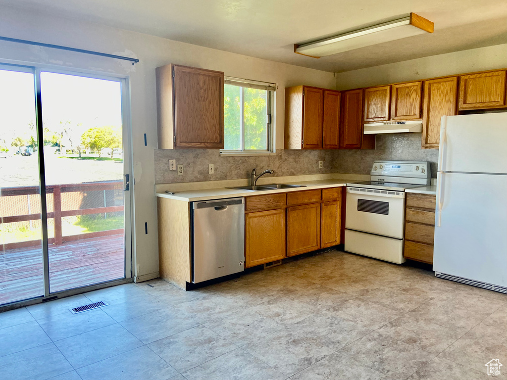 Kitchen featuring backsplash, sink, white appliances, and light tile floors