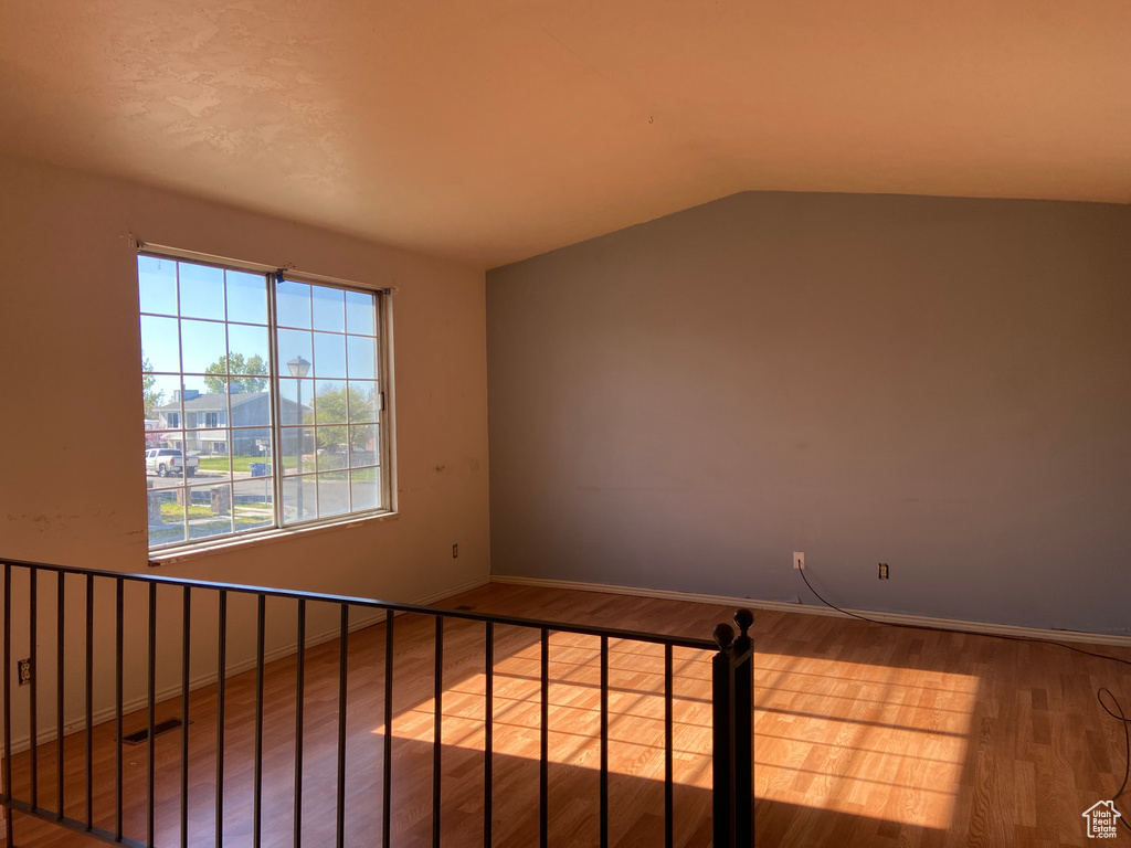 Empty room with vaulted ceiling and hardwood / wood-style floors