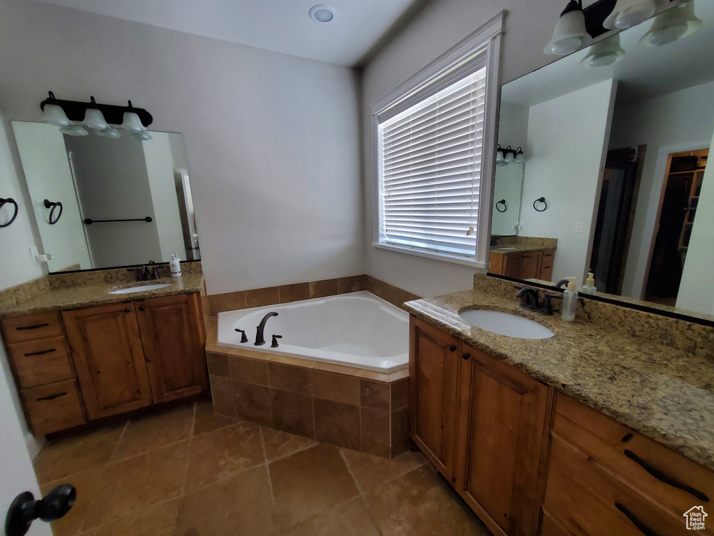 Bathroom with double vanity, tiled tub, and tile floors