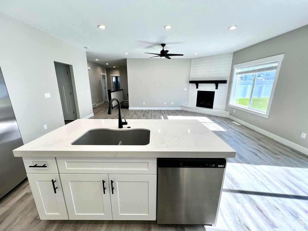 Kitchen with light hardwood / wood-style floors, stainless steel appliances, a large fireplace, and an island with sink