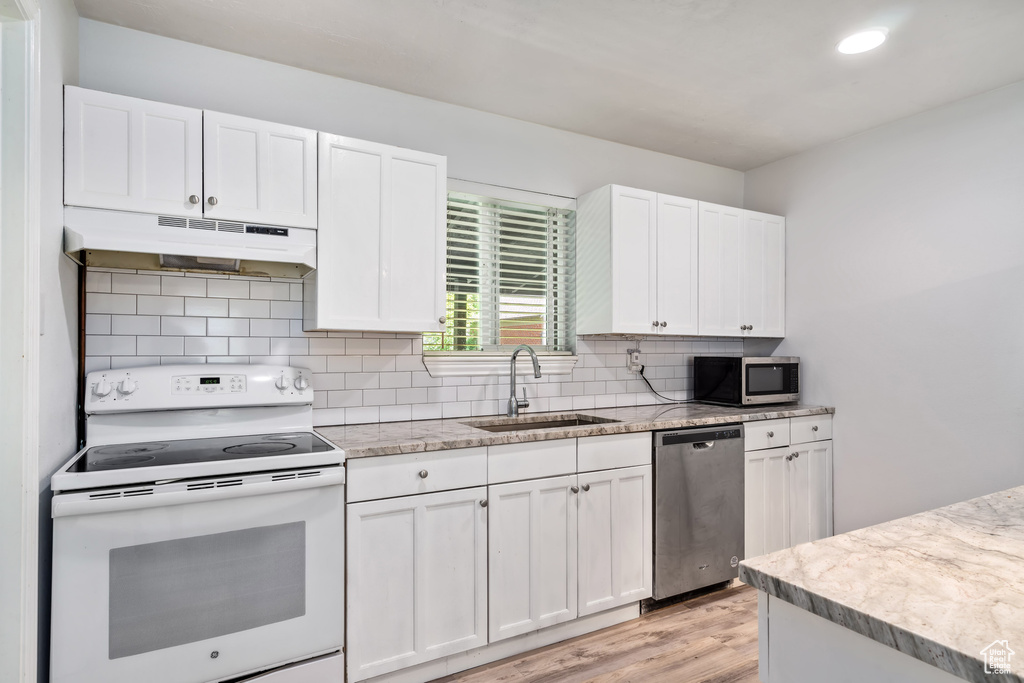 Kitchen with white cabinets, appliances with stainless steel finishes, backsplash, and light wood-type flooring