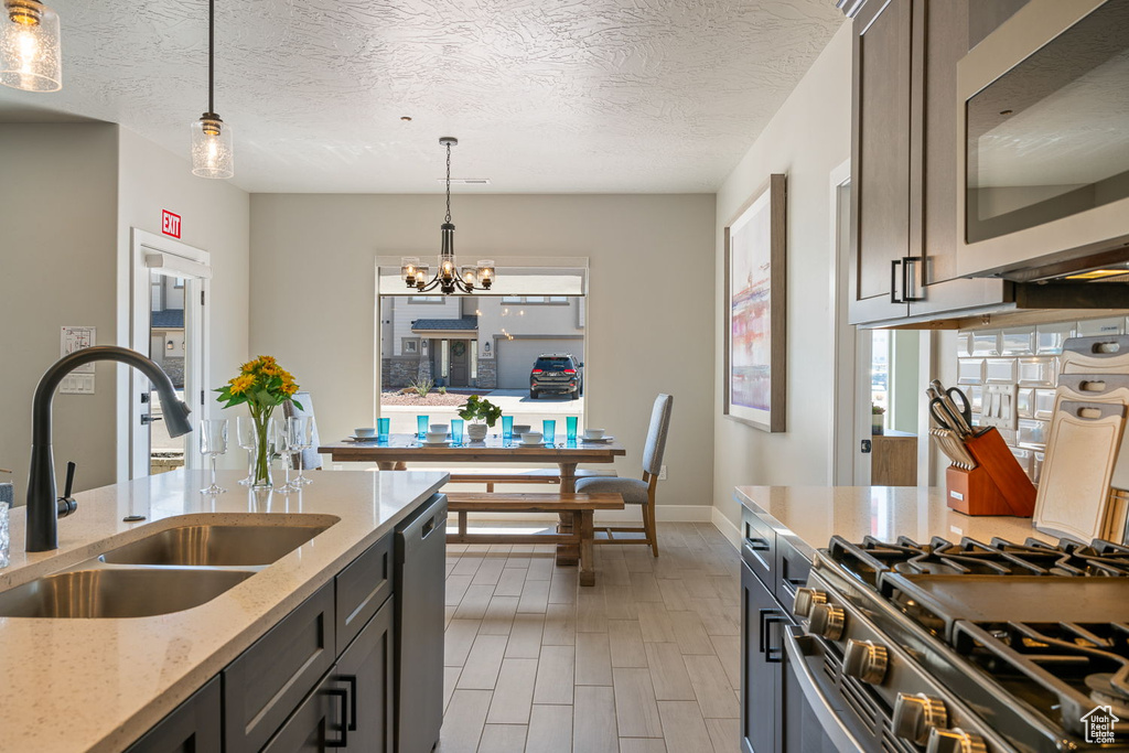 Kitchen featuring a textured ceiling, sink, stainless steel appliances, pendant lighting, and light stone countertops