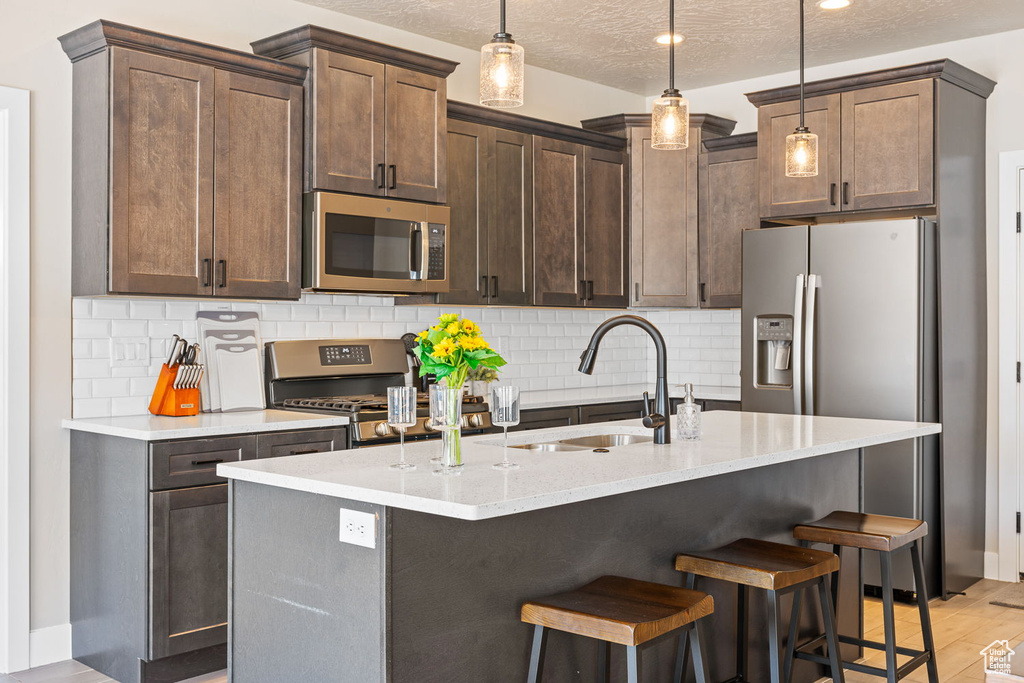 Kitchen featuring decorative light fixtures, appliances with stainless steel finishes, light hardwood / wood-style floors, tasteful backsplash, and sink