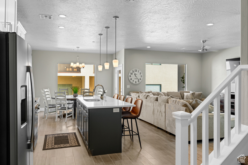 Kitchen with decorative light fixtures, stainless steel refrigerator with ice dispenser, light hardwood / wood-style flooring, white cabinetry, and sink