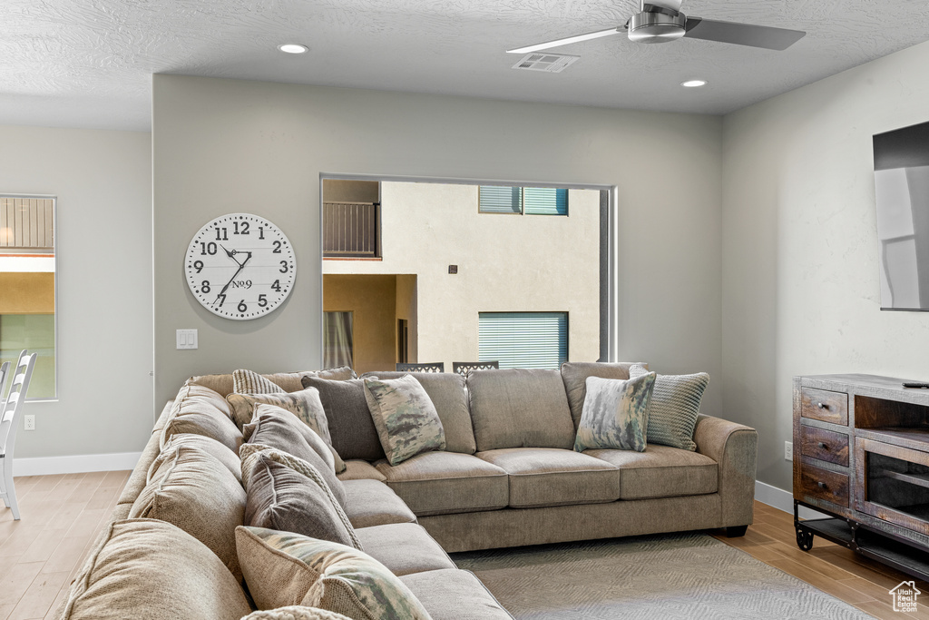 Living room featuring a textured ceiling, ceiling fan, and light wood-type flooring