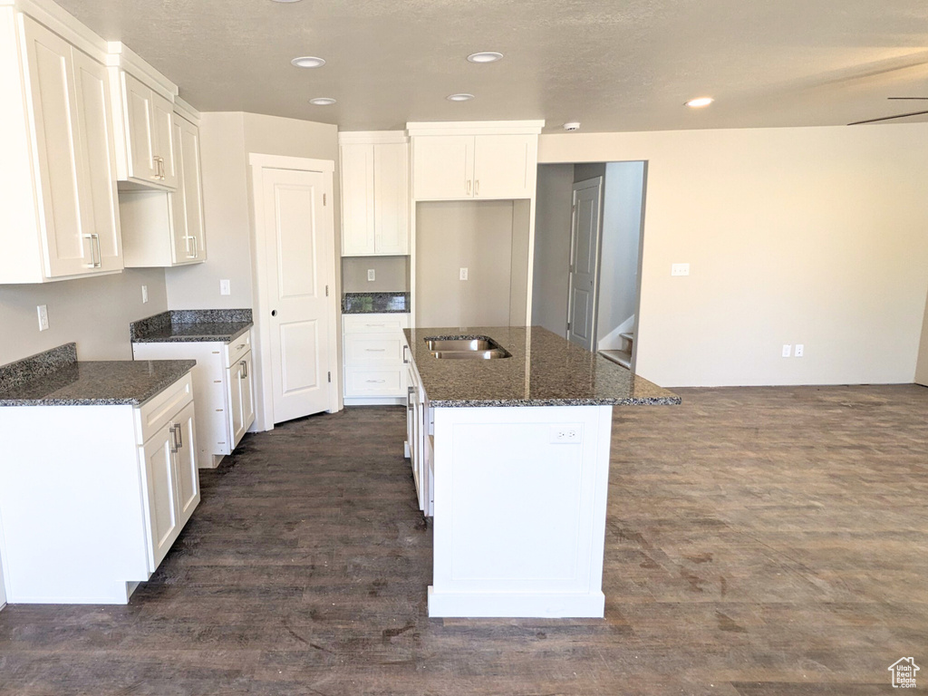 Kitchen featuring dark stone countertops, white cabinets, a kitchen island, dark hardwood / wood-style floors, and sink