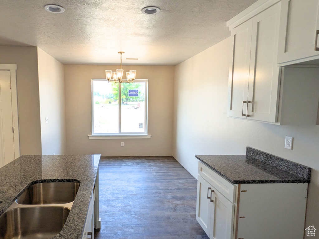 Kitchen featuring dark stone counters, white cabinetry, an inviting chandelier, and hardwood / wood-style floors