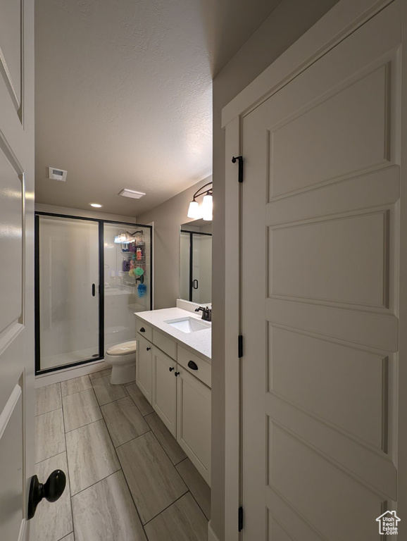 Bathroom featuring a shower with door, vanity, and toilet