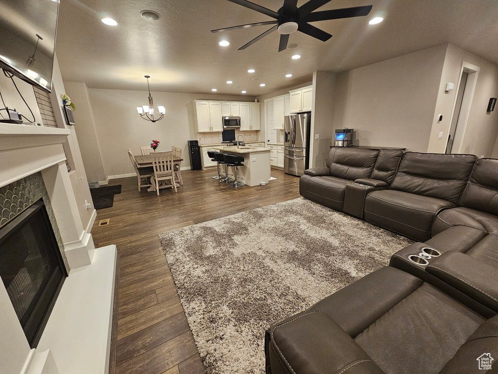 Living room featuring ceiling fan with notable chandelier, sink, and dark wood-type flooring