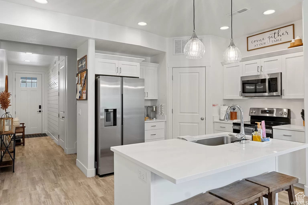 Kitchen featuring a kitchen island with sink, hanging light fixtures, light hardwood / wood-style flooring, white cabinetry, and stainless steel appliances