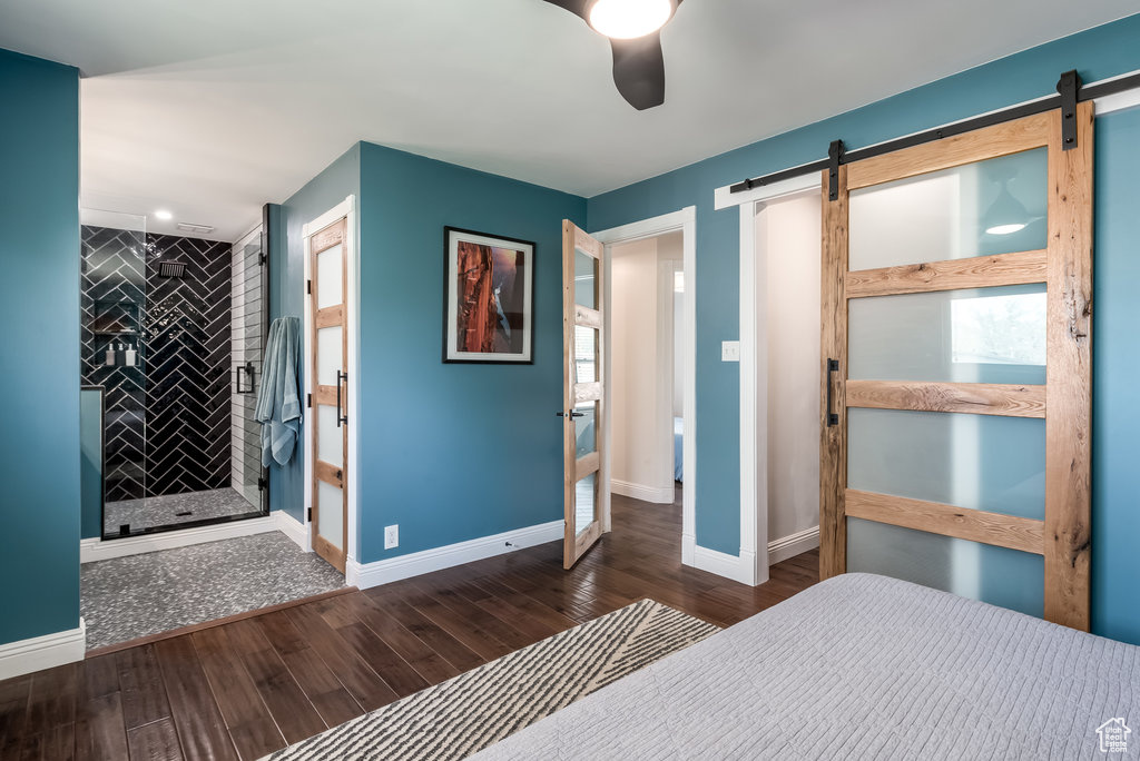 Bedroom featuring dark hardwood / wood-style floors, ceiling fan, ensuite bathroom, and a barn door