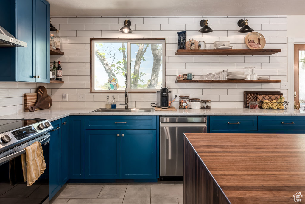 Kitchen with blue cabinetry, appliances with stainless steel finishes, light tile flooring, tasteful backsplash, and sink