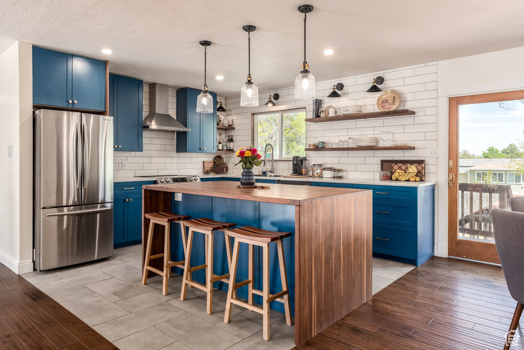 Kitchen featuring backsplash, butcher block countertops, light hardwood / wood-style floors, wall chimney exhaust hood, and stainless steel fridge