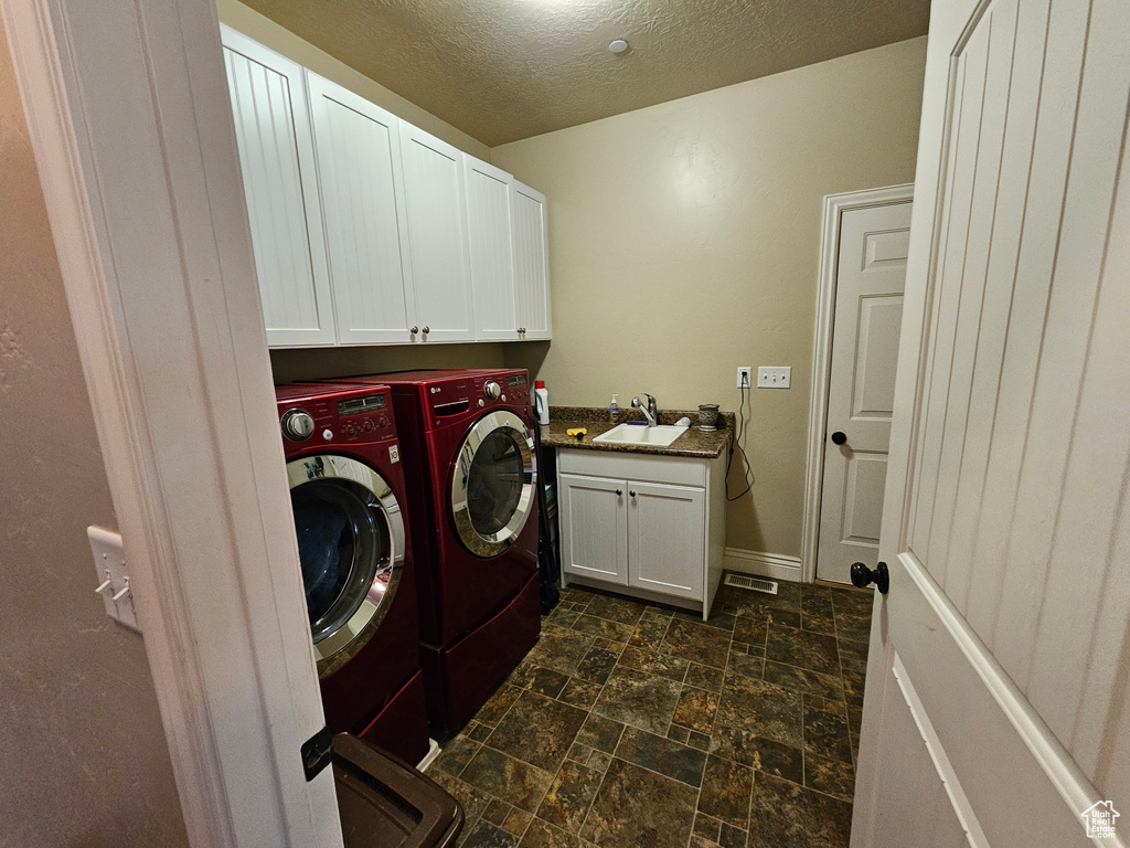 Washroom with dark tile floors, cabinets, a textured ceiling, sink, and separate washer and dryer