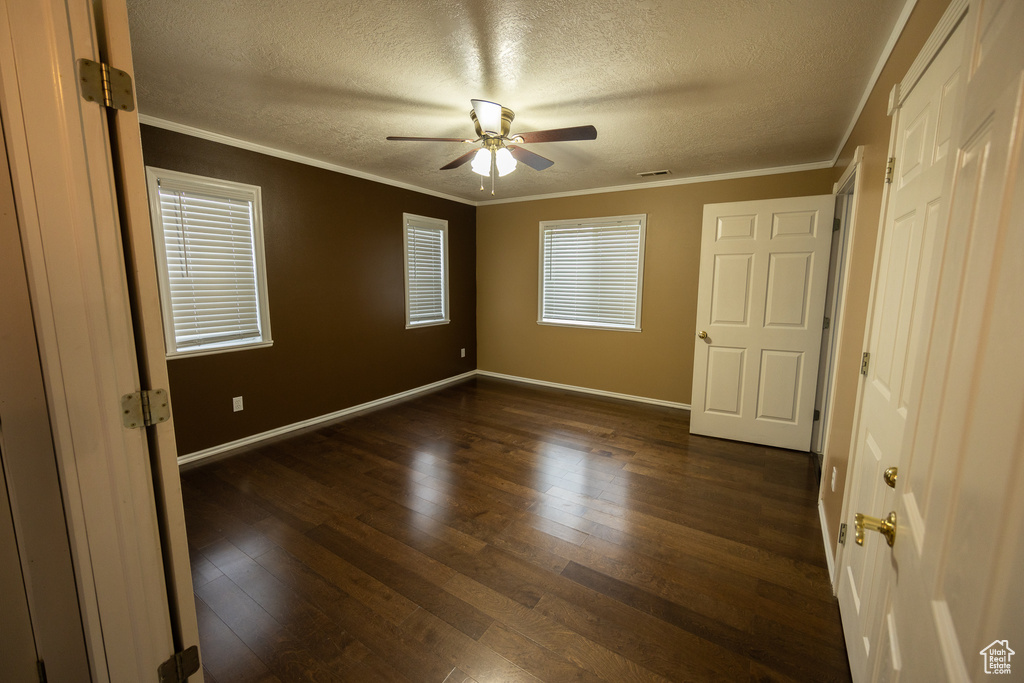 Empty room featuring dark hardwood / wood-style floors, ceiling fan, crown molding, and a textured ceiling