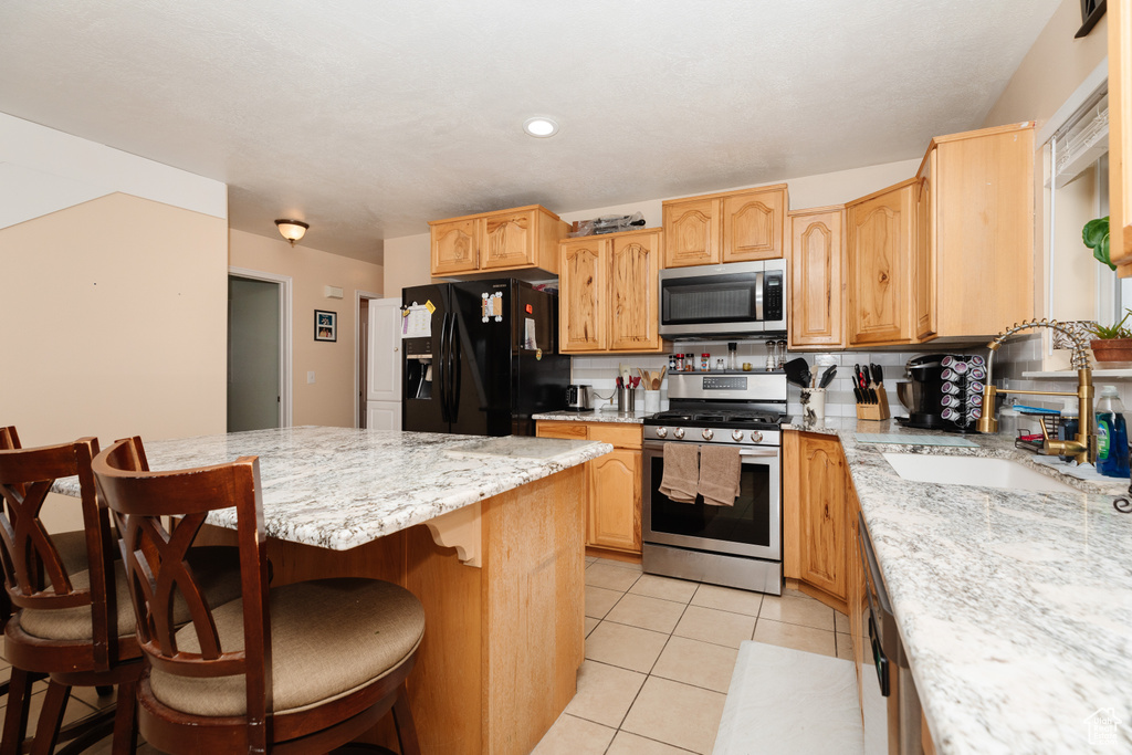 Kitchen with light tile floors, a kitchen bar, sink, tasteful backsplash, and stainless steel appliances