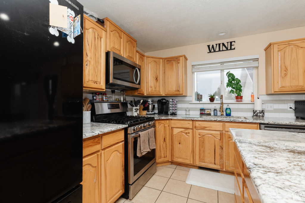 Kitchen with appliances with stainless steel finishes, backsplash, light tile flooring, light stone counters, and sink