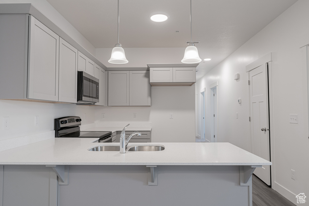 Kitchen with a breakfast bar, dark hardwood / wood-style floors, sink, pendant lighting, and stainless steel appliances