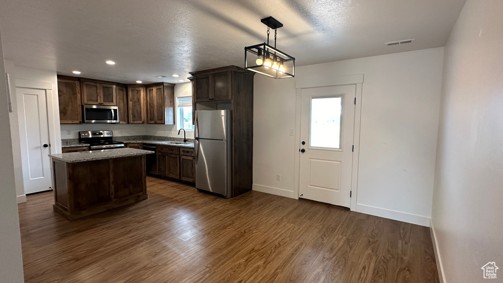Kitchen featuring appliances with stainless steel finishes, hanging light fixtures, sink, dark hardwood / wood-style flooring, and a center island