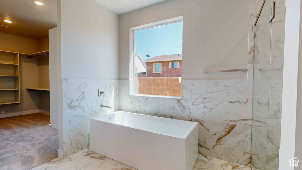 Bathroom featuring a wealth of natural light, separate shower and tub, tile floors, and tile walls