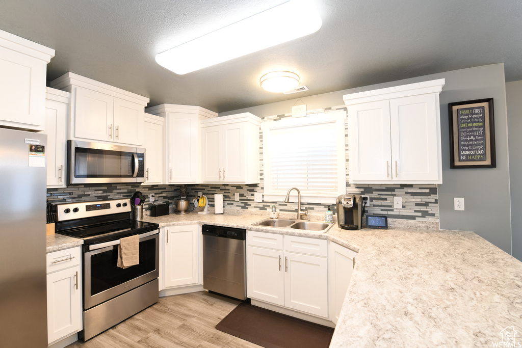 Kitchen featuring backsplash, stainless steel appliances, light hardwood / wood-style floors, white cabinetry, and sink
