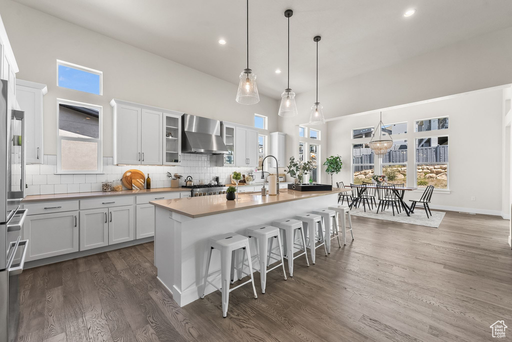 Kitchen featuring wall chimney exhaust hood, dark wood-type flooring, hanging light fixtures, and backsplash