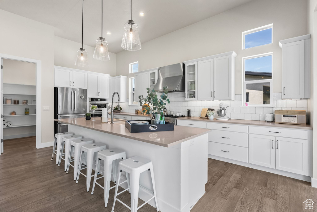 Kitchen with wall chimney exhaust hood, appliances with stainless steel finishes, dark hardwood / wood-style floors, and backsplash