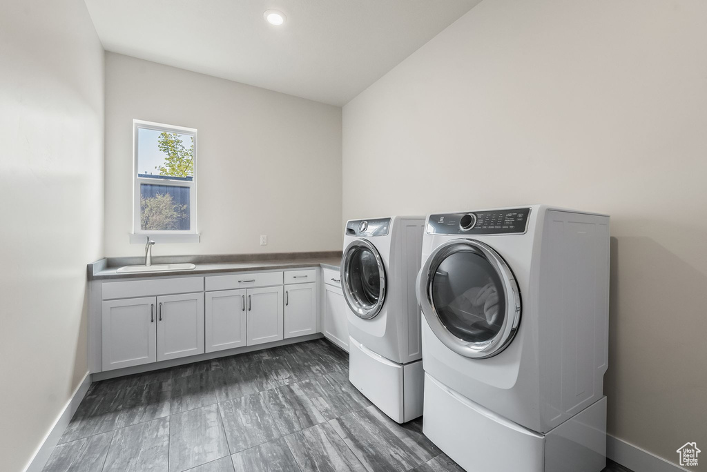 Washroom featuring washing machine and clothes dryer, cabinets, and sink