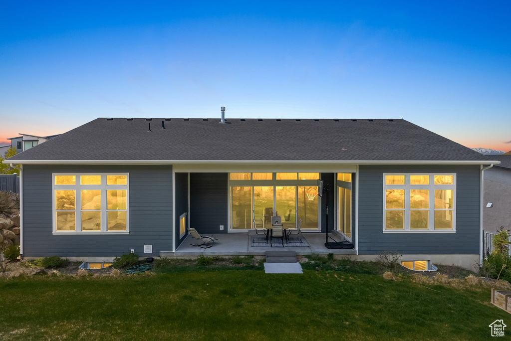 Back house at dusk with a patio area and a lawn