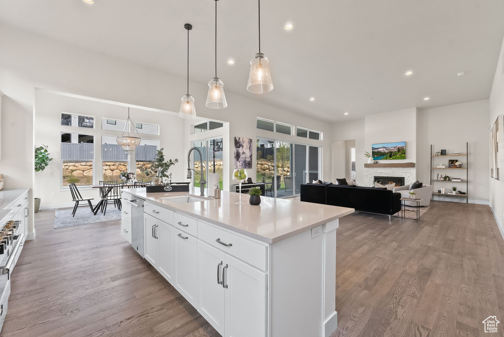 Kitchen with hanging light fixtures, a center island with sink, light hardwood / wood-style floors, dishwasher, and white cabinetry