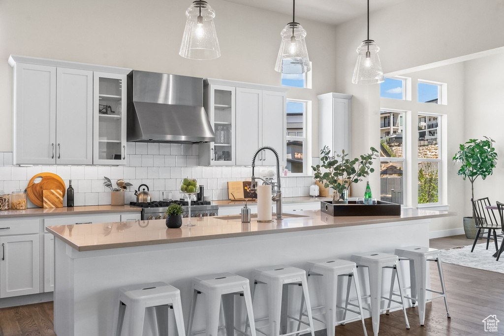 Kitchen featuring a healthy amount of sunlight, an island with sink, dark wood-type flooring, and wall chimney exhaust hood