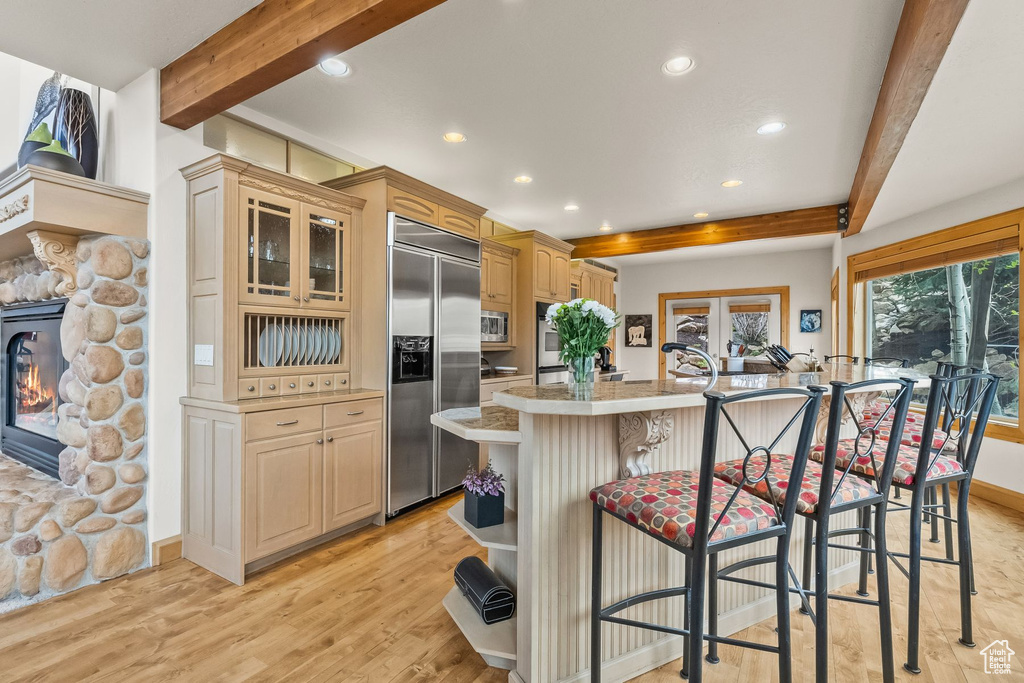 Kitchen featuring built in appliances, a fireplace, light hardwood / wood-style flooring, beam ceiling, and a breakfast bar area